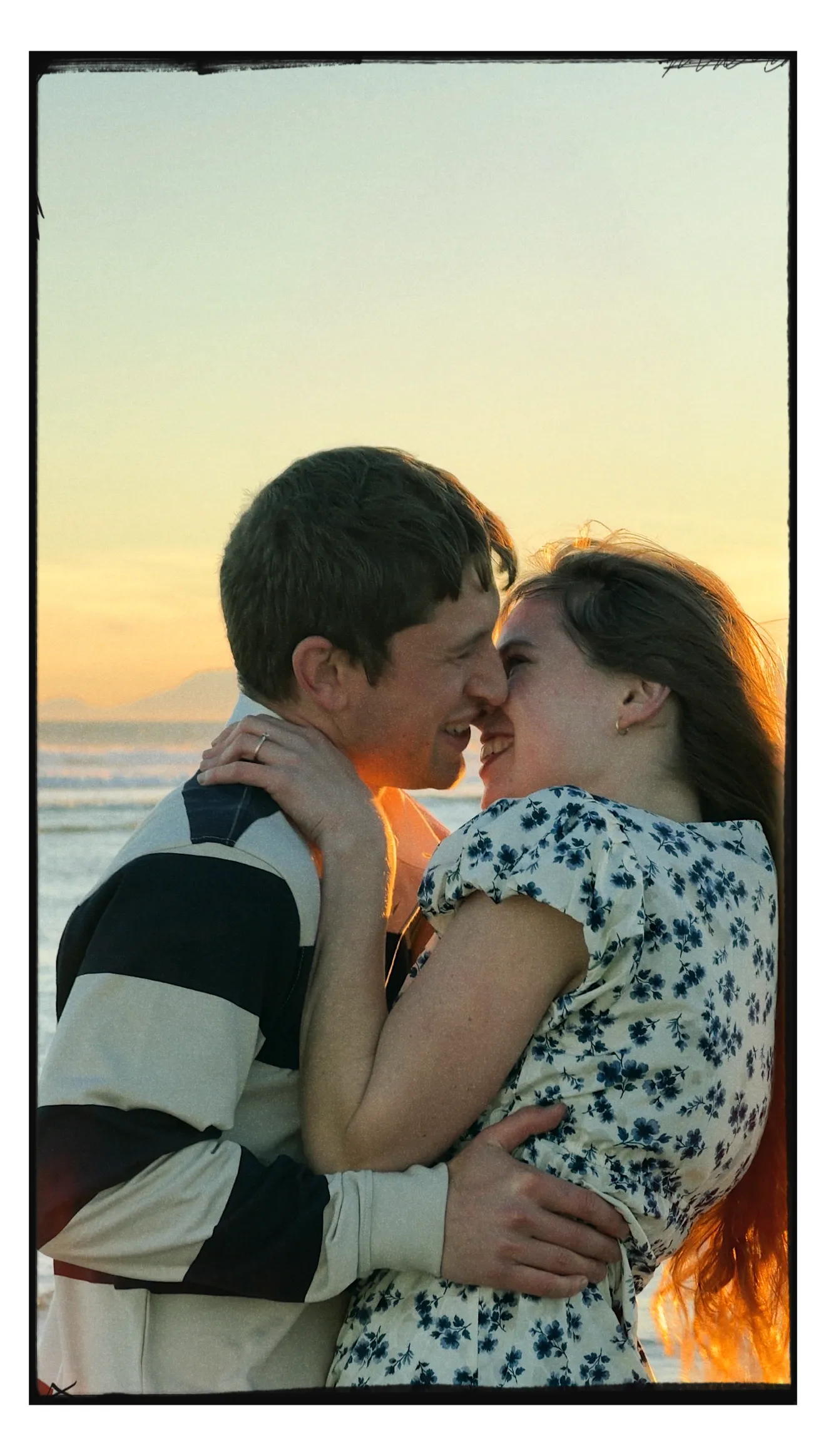 A couple close together by the sea at sunset